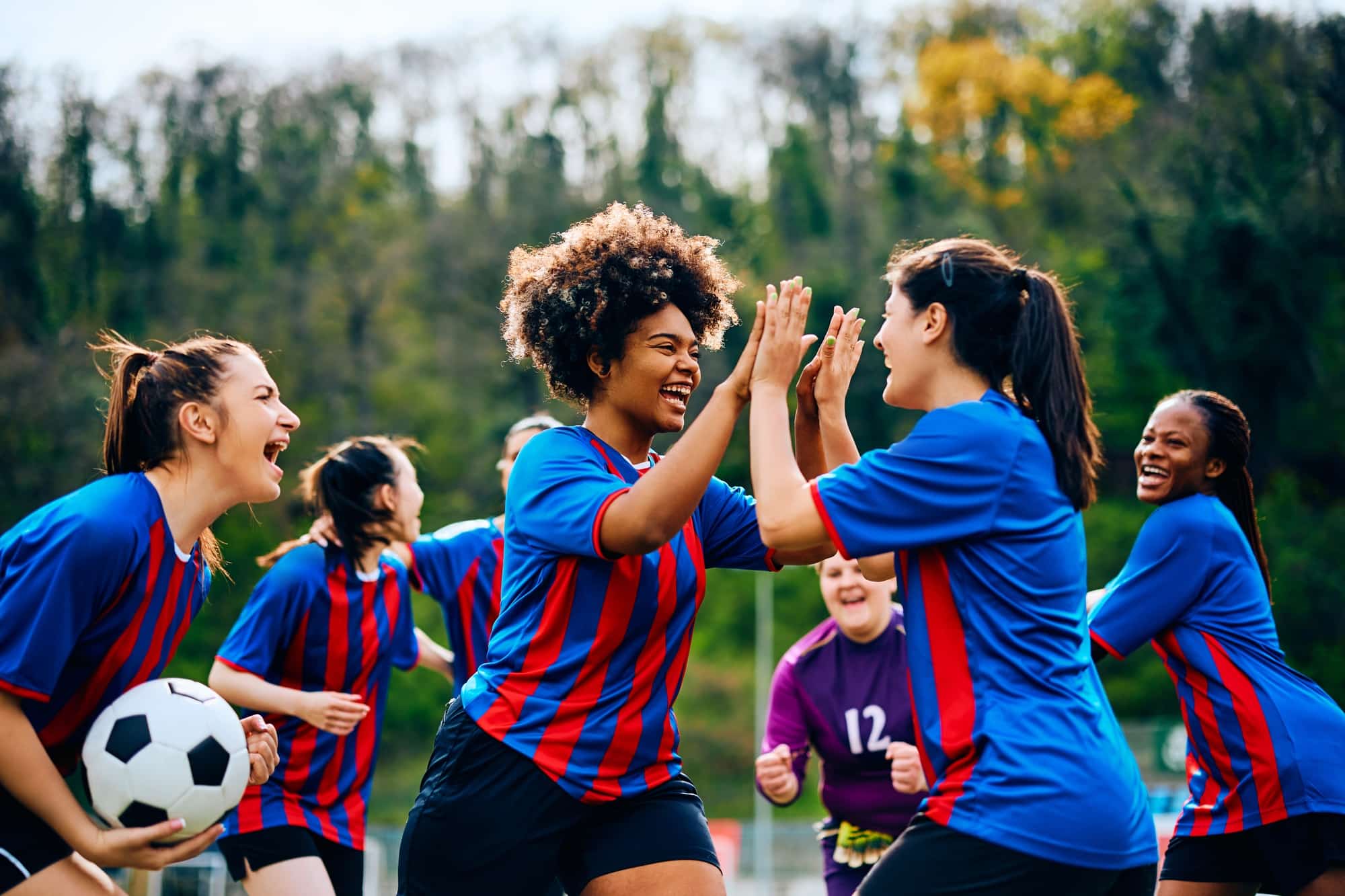 Happy women's soccer team celebrating victory after playing a match at the stadium.